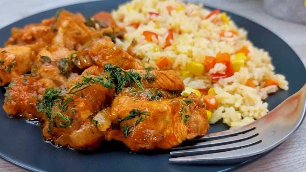 Smažené kuřecí kousky s cibulí, zdobené koprem a s přílohou rýže se zeleninou – oběd hotový!