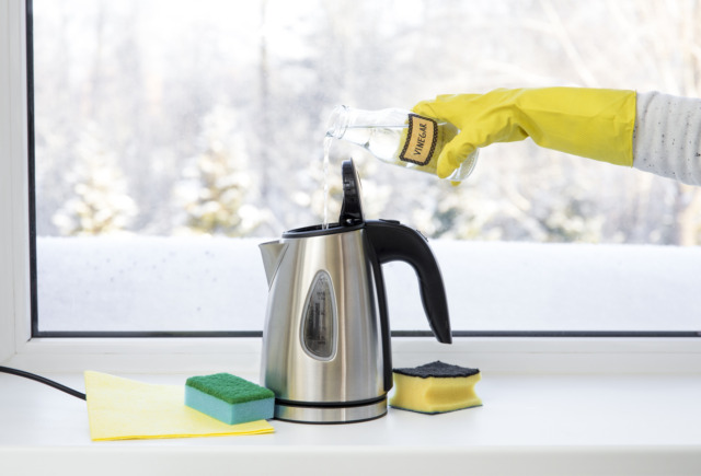 Woman pouring natural destilled acid white vinegar in electric kettle to remove boil away the limescale. Descaling a kettle, remove scale concept.
