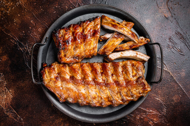 BBQ pork spare ribs St Louis with hot honey marinade in a steel tray. Dark background. Top view