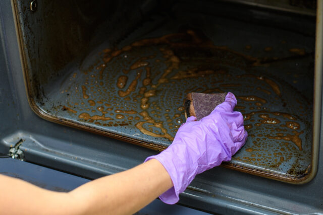 Home cleaning concept. A woman's hand washes with a sponge on a dirty oven.