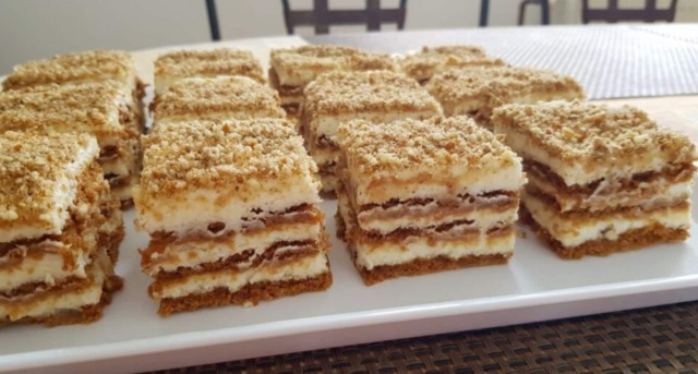 Vrstvené nepečené řezy ze sušenek Lotus Biscoff s krémem z mascarpone, posypané drcenými sušenkami a ořechy na servírovacím talíři.