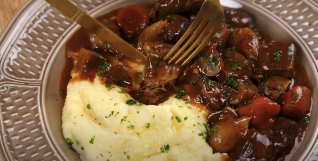 Pomalu dušené hovězí na červeném víně s kořenovou zeleninou a žampiony, podávané s jemnou bramborovou kaší