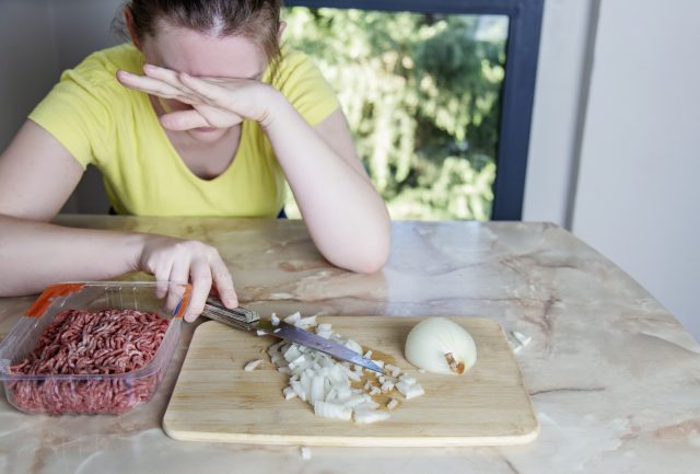 Woman cutting onion and crying, young female closed eyes