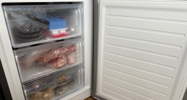 Otevřený mrazák se třemi šuplíky plnými potravin.