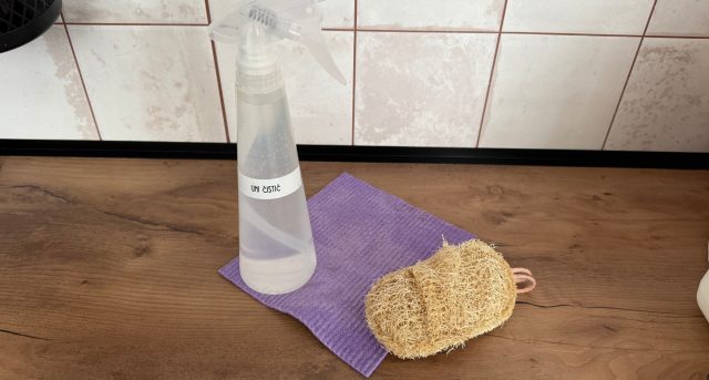Rozprašovač s čisticím prostředkem, přírodní houbička a utěrka na kuchyňské lince.
