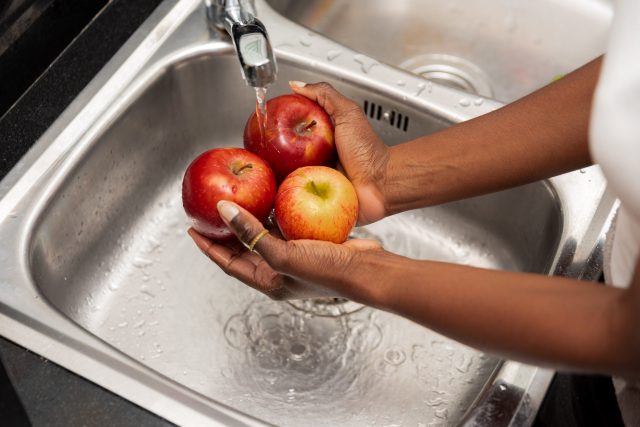 close up of Hands Rinsing Red Apples Under Tap Water in a Stainless Steel Kitchen Sink