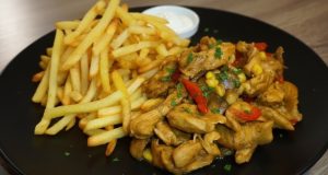 Šťavnatá kuřecí směs s paprikou a kukuřicí podávaná s křupavými hranolky na černém talíři