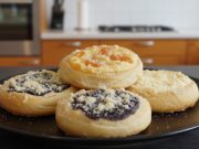 ALT text: „Domácí kynuté koláče s tvarohem, borůvkami a meruňkami sypané zlatavou drobenkou na černém talíři