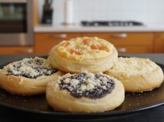 ALT text: „Domácí kynuté koláče s tvarohem, borůvkami a meruňkami sypané zlatavou drobenkou na černém talíři