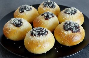 Domácí měkoučké koláčky s povidly, tvarohem a drobenkou na černém talíři.