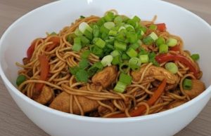 Čínské nudle s kuřecím a zeleninou: Moje vychytávka na autentickou chuť bez podlévání Pohled na pánev s restovanými čínskými nudlemi, kuřecím masem v teriyaki omáčce, mrkví, pórkem a kapií.