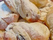 Kynuté motánky s tvarohem a rumovými rozinkami: Nadýchaný luxus k ranní kávě Pocukrované kynuté motánky na talíři.