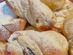 Kynuté motánky s tvarohem a rumovými rozinkami: Nadýchaný luxus k ranní kávě Pocukrované kynuté motánky na talíři.