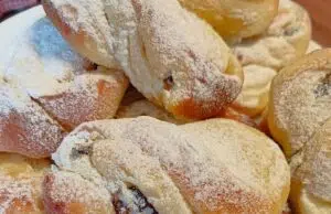 Kynuté motánky s tvarohem a rumovými rozinkami: Nadýchaný luxus k ranní kávě Pocukrované kynuté motánky na talíři.