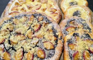 Poctivé kynuté koláče s tvarohem, mákem a slívami Dva velké a několik menších čerstvě upečených kynutých koláčů na pečicím papíře. Zdobené jsou makovou a tvarohovou náplní, plátky slív a bohatě posypané máslovou drobenkou a moučkovým cukrem.