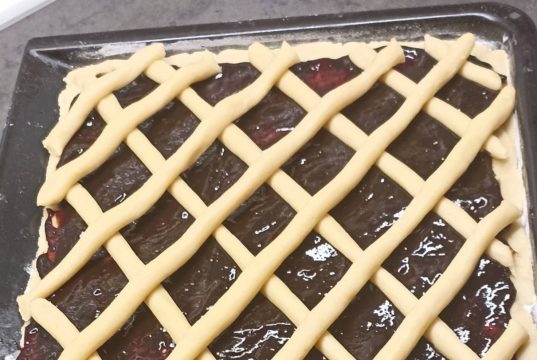 Tradiční mřížkový koláč s povidly: Bleskové křehké těsto z robotu Čerstvě upečený křehký koláč na plechu s bohatou vrstvou tmavých švestkových povidel, který je na povrchu ozdobený pravidelnou mřížkou ze zlatavě upečeného těsta.