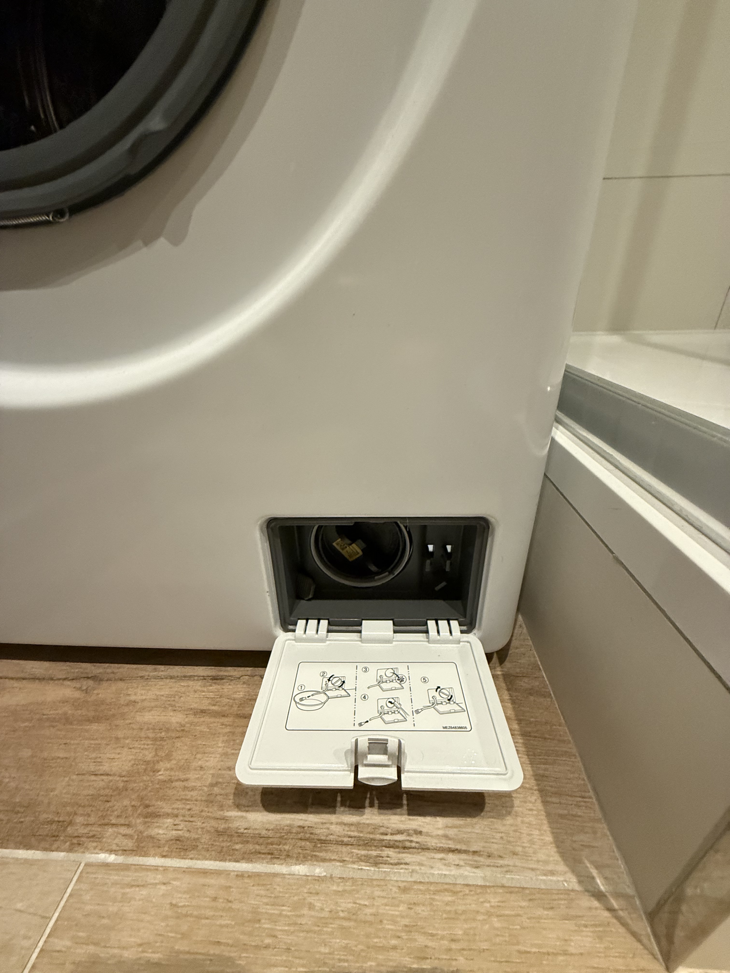 Detail otevřených servisních dvířek filtru nebo odtoku v dolní části pračky.