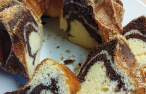 Vláčná tvarohová bábovka s kakaovým mramorováním: Recept na nejjemnější dezert Domácí mramorová bábovka s tvarohem na bílém talíři, nakrájená na plátky, s viditelnou jemnou strukturou a kakaovým vzorem na dřevěném stole.