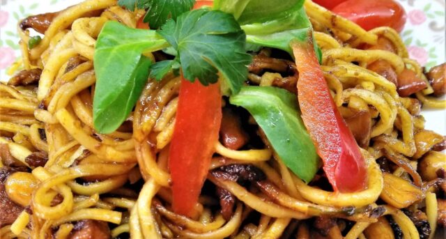 Restované čínské nudle se zeleninou, paprikou a bylinkami na talíři.