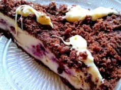 Čokoládový drobenkový koláč s mascarpone a borůvkami: Luxusní dezert bez námahy Kousek čokoládového drobenkového koláče s krémovou vrstvou a polevou.“