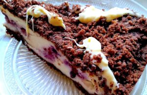 Čokoládový drobenkový koláč s mascarpone a borůvkami: Luxusní dezert bez námahy Kousek čokoládového drobenkového koláče s krémovou vrstvou a polevou.“