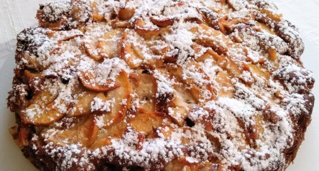 Domácí jablečný koláč posypaný moučkovým cukrem s plátky jablek.