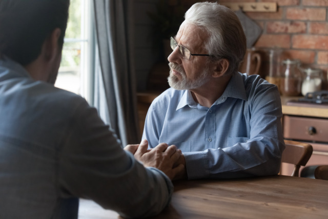 Attentive grownup kid talk hold hands of sad senior father