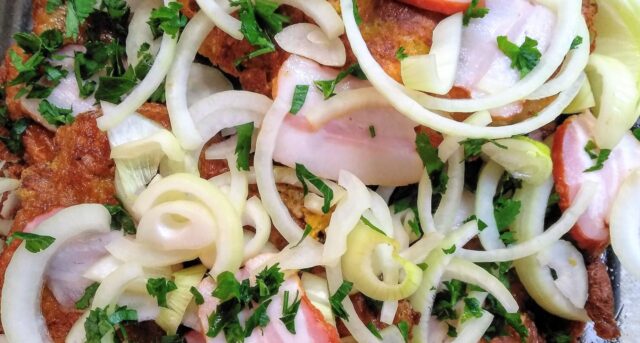 Zapečené řízky s cibulí a bylinkami, podávané s čerstvou zeleninou.