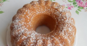 Nadýchaná pomerančová bábovka: Vláčná a voňavá pochoutka s nádechem citrusů Detailní řez nadýchanou pomerančovou bábovkou, jemně pocukrovanou a zdobenou plátky čerstvého pomeranče na bílém talířku.