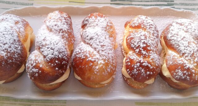 Kynuté buchty plněné krémem, posypané moučkovým cukrem.