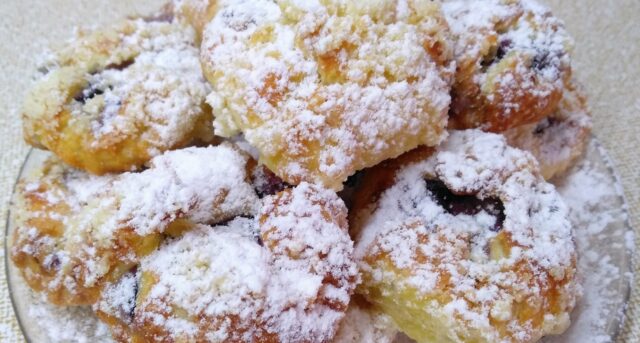 Malé koláčky s ovocem a drobenkou, bohatě posypané moučkovým cukrem.