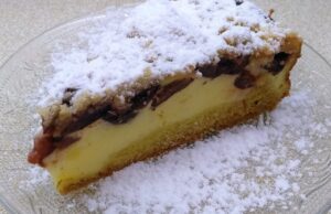 Linecký koláč s bohatou tvarohovou náplní, švestkami a skořicovou drobenkou Řez tvarohového koláče s ovocem a drobenkou, posypaný cukrem.