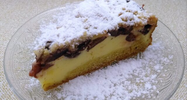 Řez tvarohového koláče s ovocem a drobenkou, posypaný cukrem.