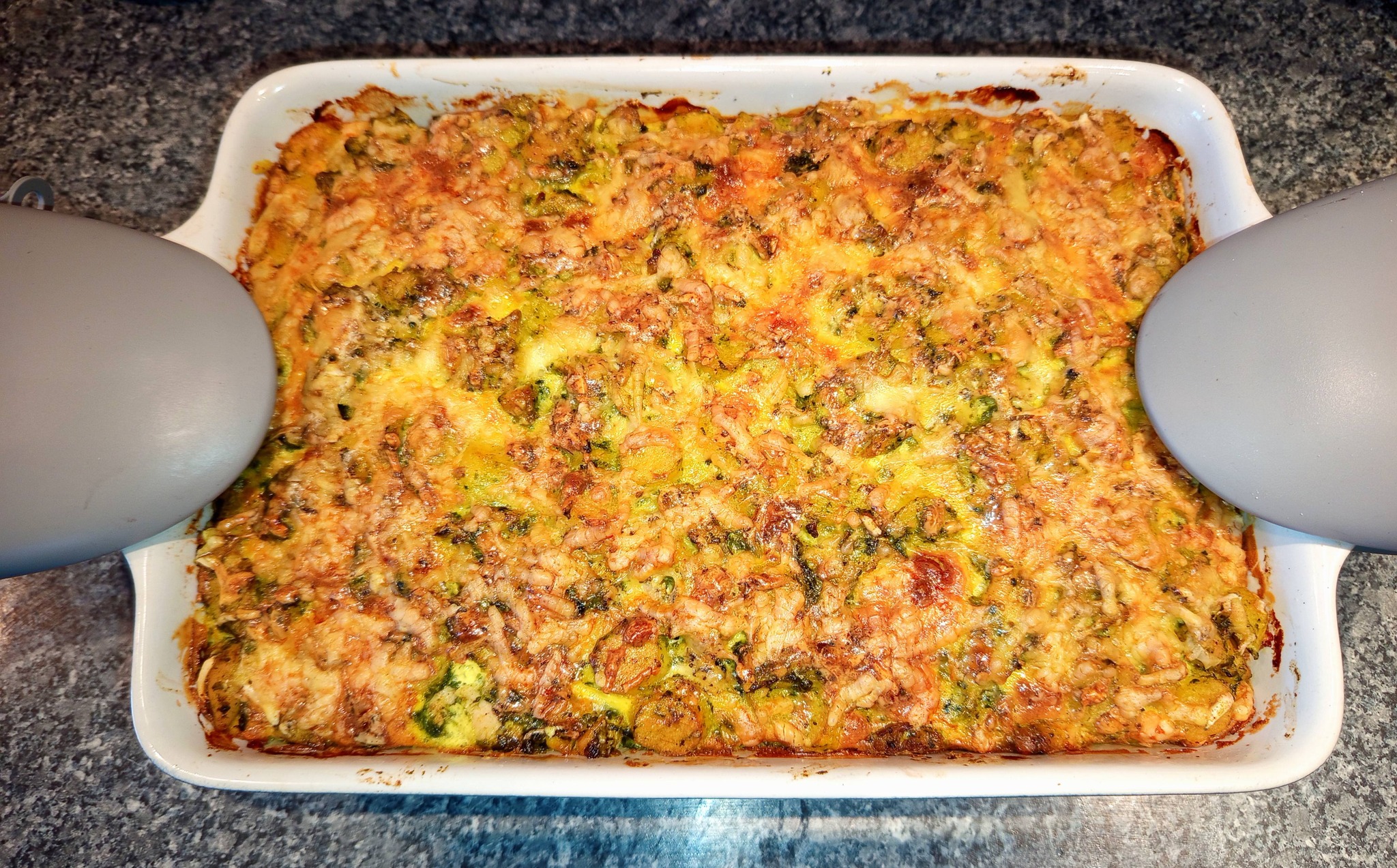 Keramická zapékací mísa s upečenými domácími bramborovými gnocchi, kuřecím masem a špenátem, s rozpuštěnou nivou a zlatavou smetanovou kůrkou.