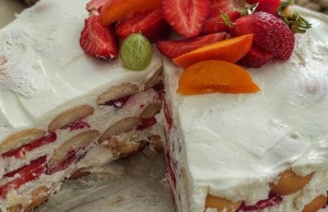 Nepečený smetanový dort s jahodami a mascarpone: Osvěžující bomba, která se rozplývá na jazyku Celkový pohled na nepečený jahodový dort s bílým smetanovým krémem, bohatě zdobený čerstvými jahodami v kulaté formě.