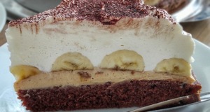 Luxusní banánový dort s arašídovým máslem a mascarpone: Chuťová exploze v každém soustu Detailní řez banánovým dortem s viditelnými vrstvami tmavého arašídového krému, celými banány a vysokou čepicí bílého mascarpone krému.