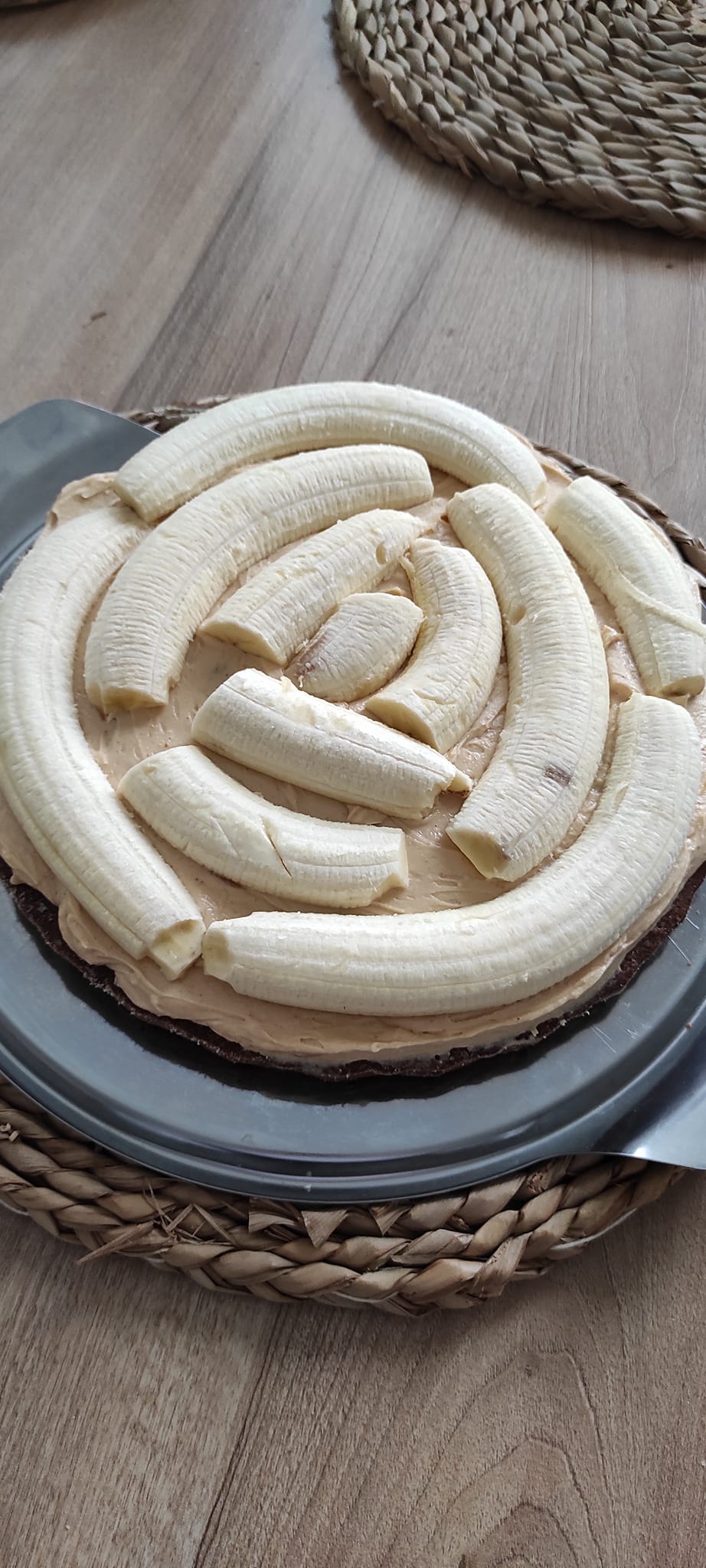 Detailní řez banánovým dortem s viditelnými vrstvami tmavého arašídového krému, celými banány a vysokou čepicí bílého mascarpone krému.