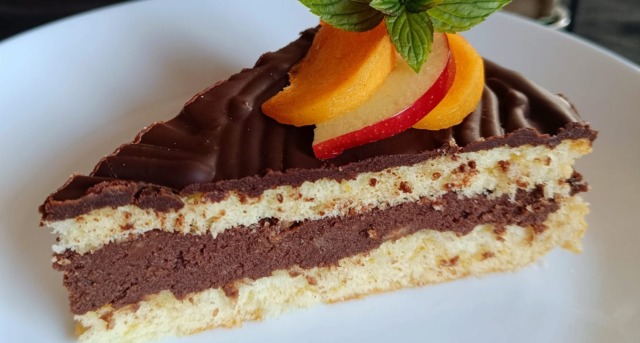 nugátový dortík Detailní záběr na řez nugátovým dortem s nadýchaným světlým piškotem, vysokou vrstvou tmavé ořechové náplně a lesklou čokoládovou polevou.