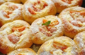 Vláčné kynuté koláče s vanilkovým pudinkem, meruňkami a rumovým máslem Plech plný zlatavých kulatých kynutých koláčů s pudinkem, zářivě oranžovými meruňkami a křupavou drobenkou, lesklé potřené okraje.