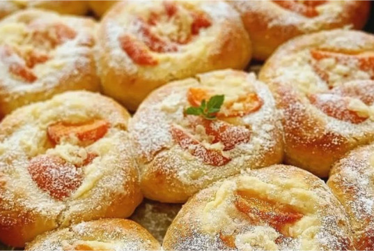 Vláčné kynuté koláče s vanilkovým pudinkem, meruňkami a rumovým máslem Plech plný zlatavých kulatých kynutých koláčů s pudinkem, zářivě oranžovými meruňkami a křupavou drobenkou, lesklé potřené okraje.